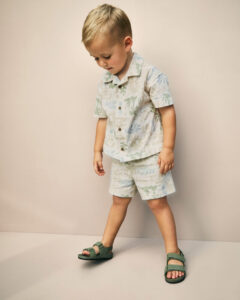 Toddler boy wearing a cream-colored tropical palm tree print matching top and shorts summer outfit set