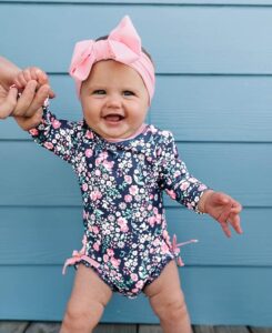 Toddler girl wearing a long sleeve floral rashguard swimsuit with full coverage for sun protection at the beach or pool