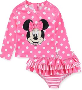 Toddler girl wearing a pink Minnie Mouse long sleeve rash guard swimsuit with polka dots and matching bottoms at the beach or pool